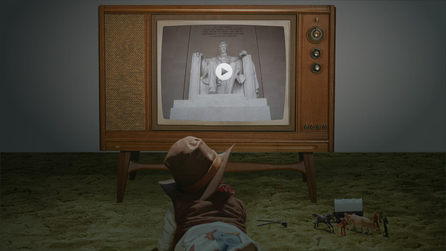 A kid dressed up as a cowboy lying on the floor watching TV with old cowboy toys
